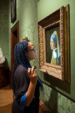 Abbie Vandivere står och tittar på tavlan Flickan med pärlöränge. Foto: Ivo Hoekstra, Mauritshuis