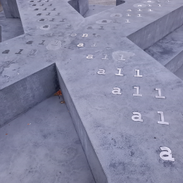 Monument i betong i form av bokstaven X liggande med text på 