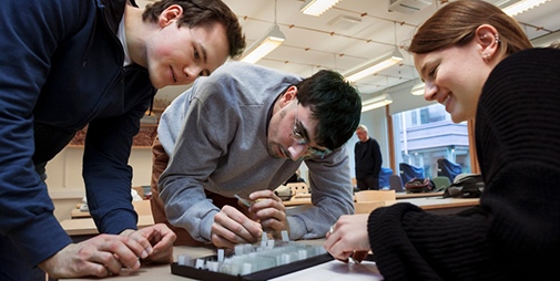 Smiling students, heads close around a sience experimet